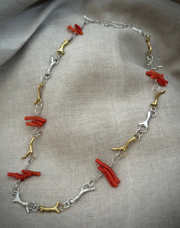 Necklace with red coral and gold and silver links on a gray fabric background