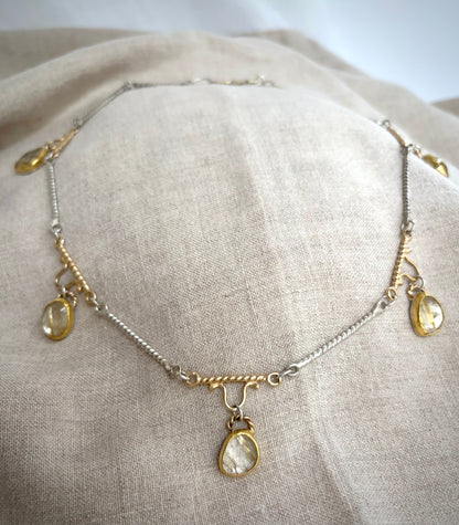 Gold and silver necklace with five golden rutile  quarts charms resting on a flax-colored fabric background