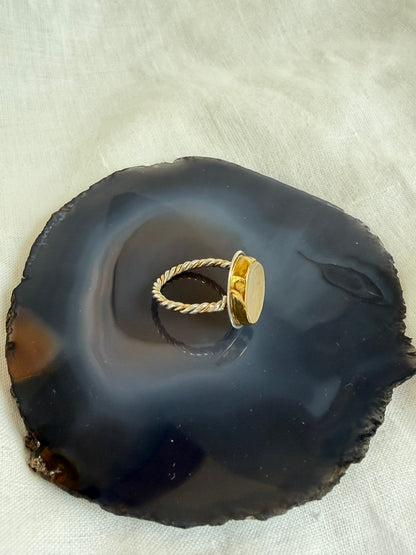 A gold and silver ring with a round bezel-set stone displayed on a polished navy blue agate slice, set against a white fabric background. The band of the ring is