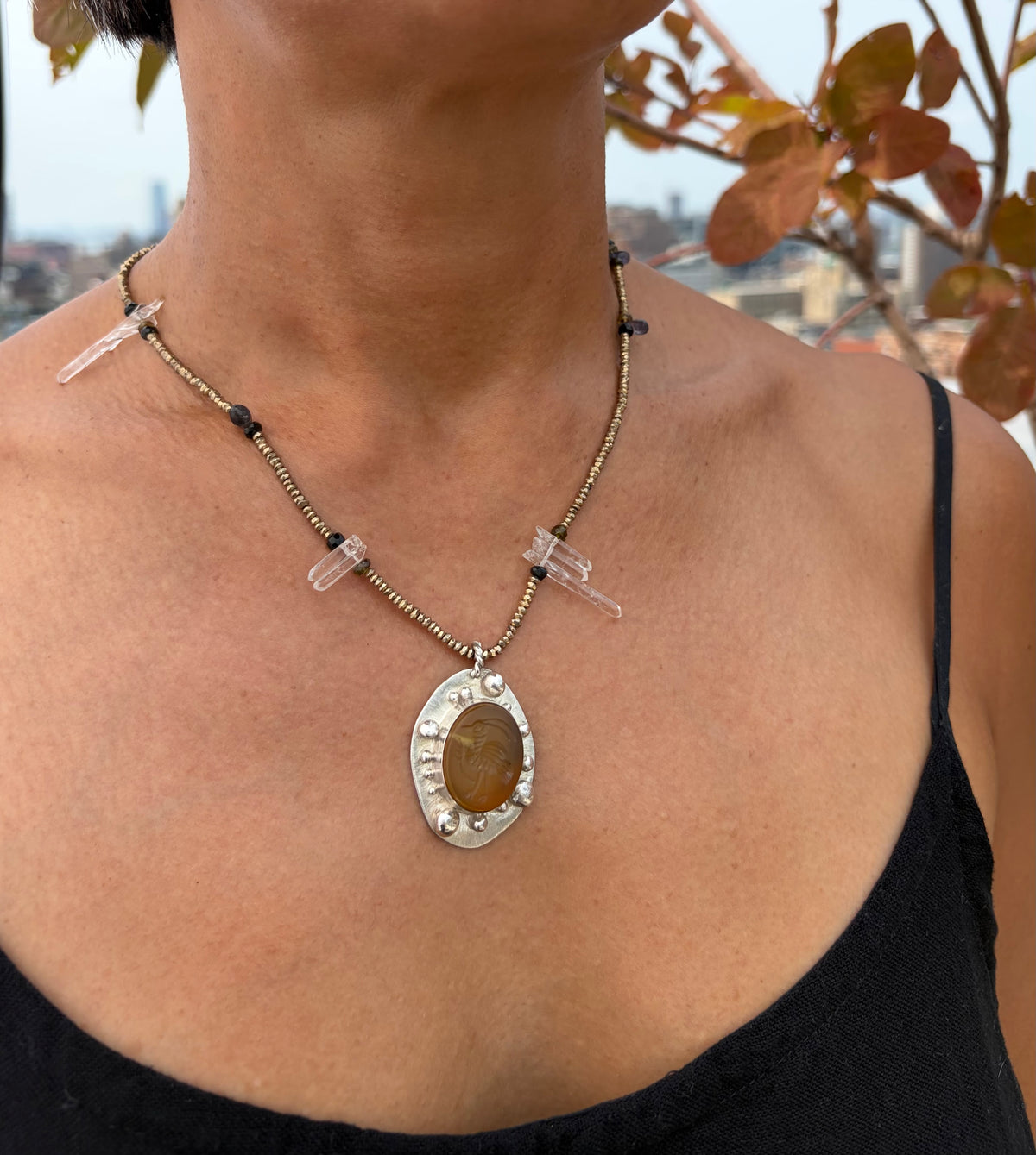 A beaded necklace with a pendant featuring a bird carved into a yellow-orange stone set in silver. A model wears the necklace with a black sundress.